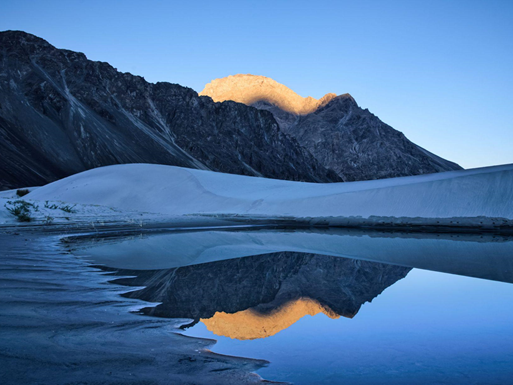 A serene mountain landscape mirrored in the calm waters of a small lake, showcasing nature's beauty and tranquility.